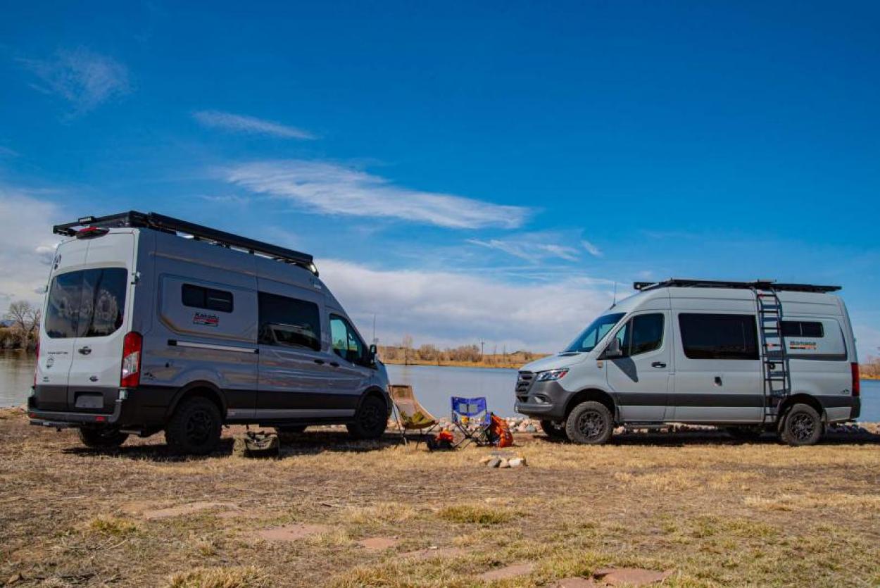 Antero Kakadu and Antero Bamaga parked facing each other in front of a blue lake under a blue, some camping supplies around