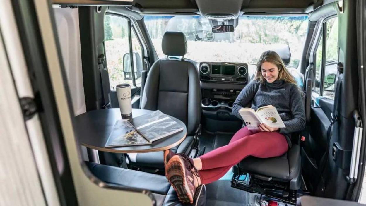 Woman reading a book in the dining area of a Winnebago Revel campervan