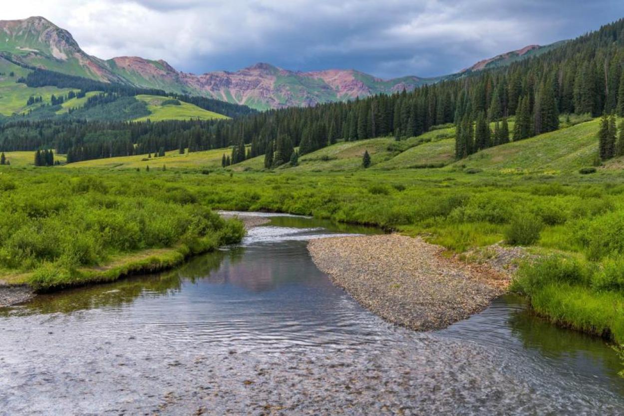 Cloudy sky and mountains in the distance, with a babbling creek up close. Taken in Grand Lake, CO