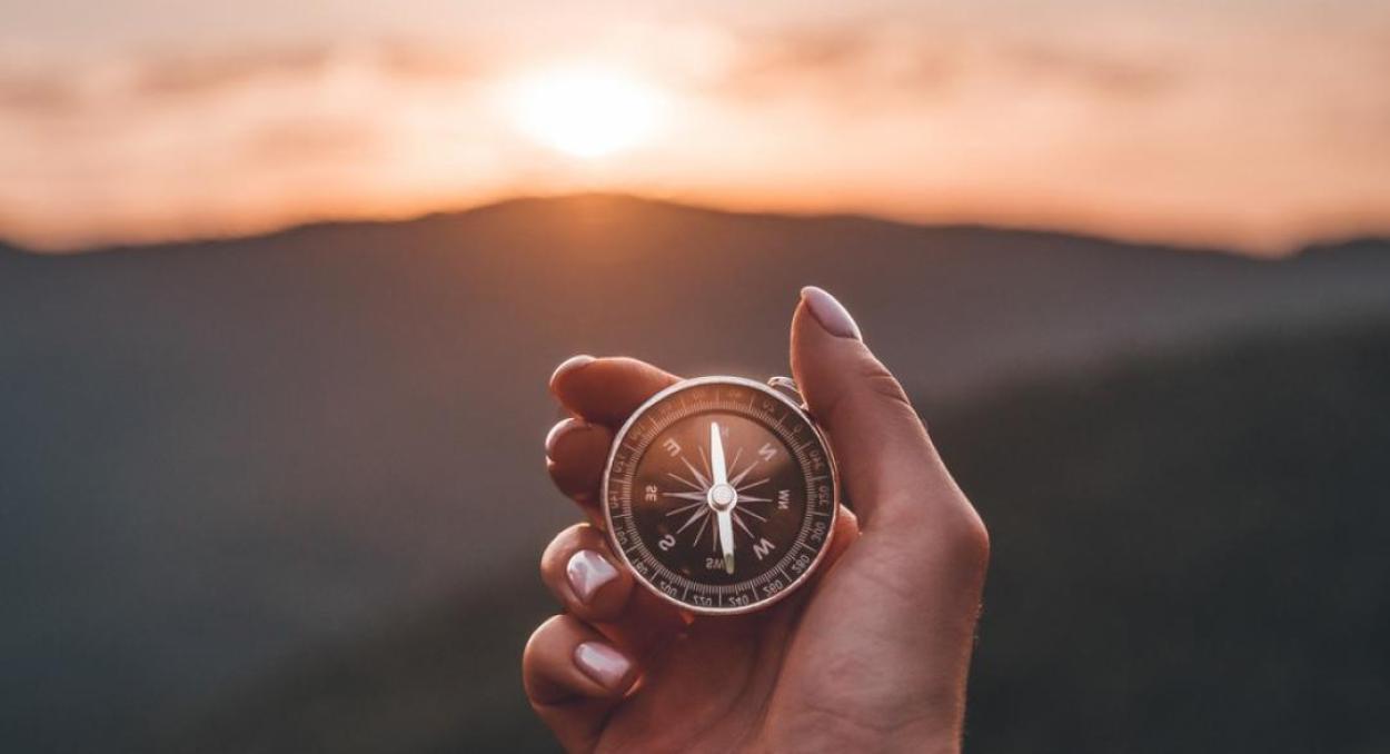 Hand holding a compass in front of a mountain scene