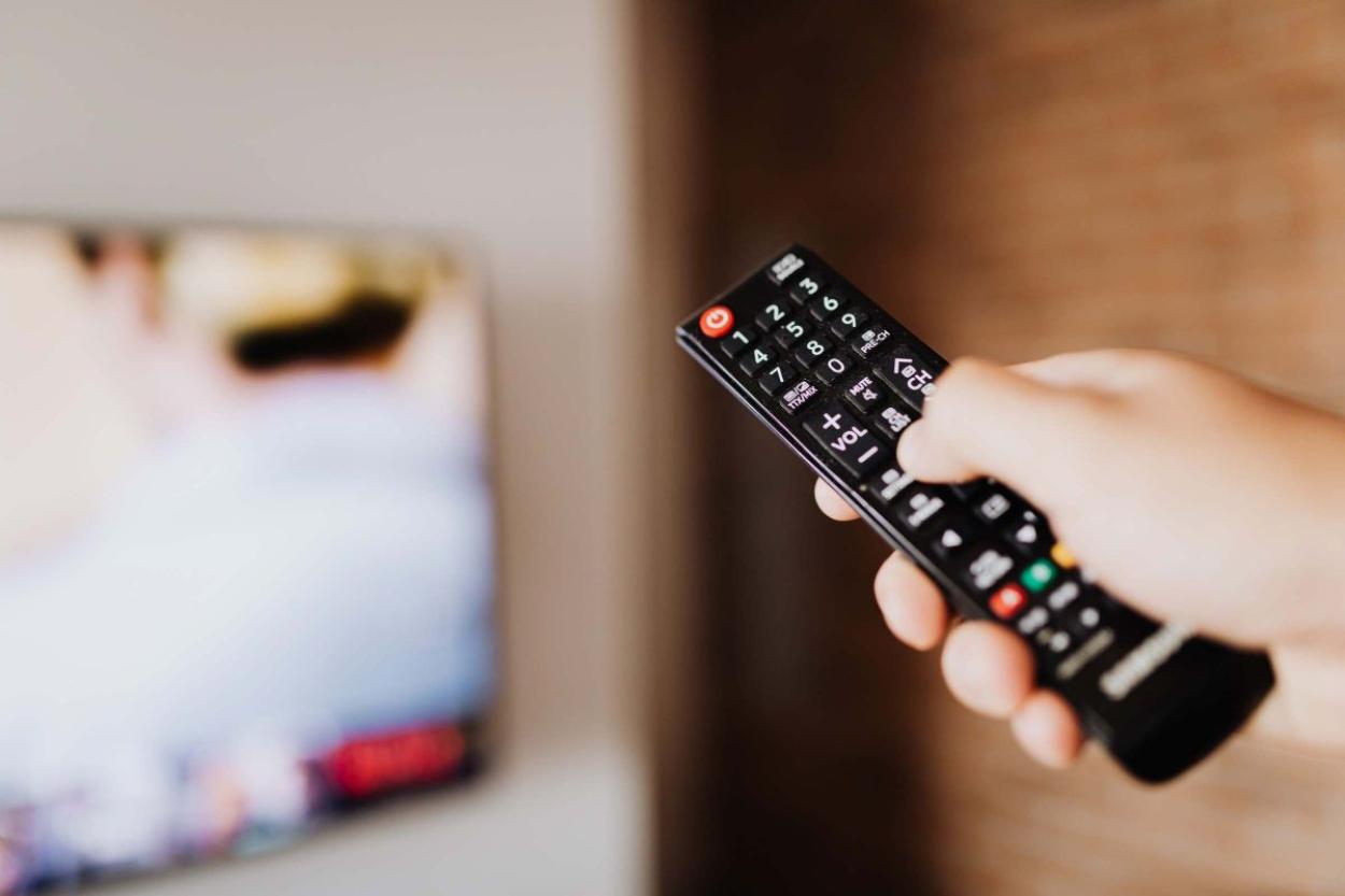 Hand holding out a television remote with a television in the background