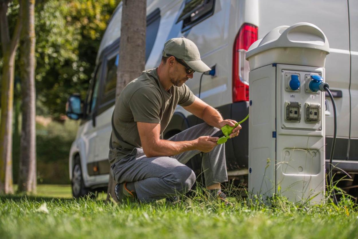 Man hooking up an electricity hookup for a campervan in a grassy area