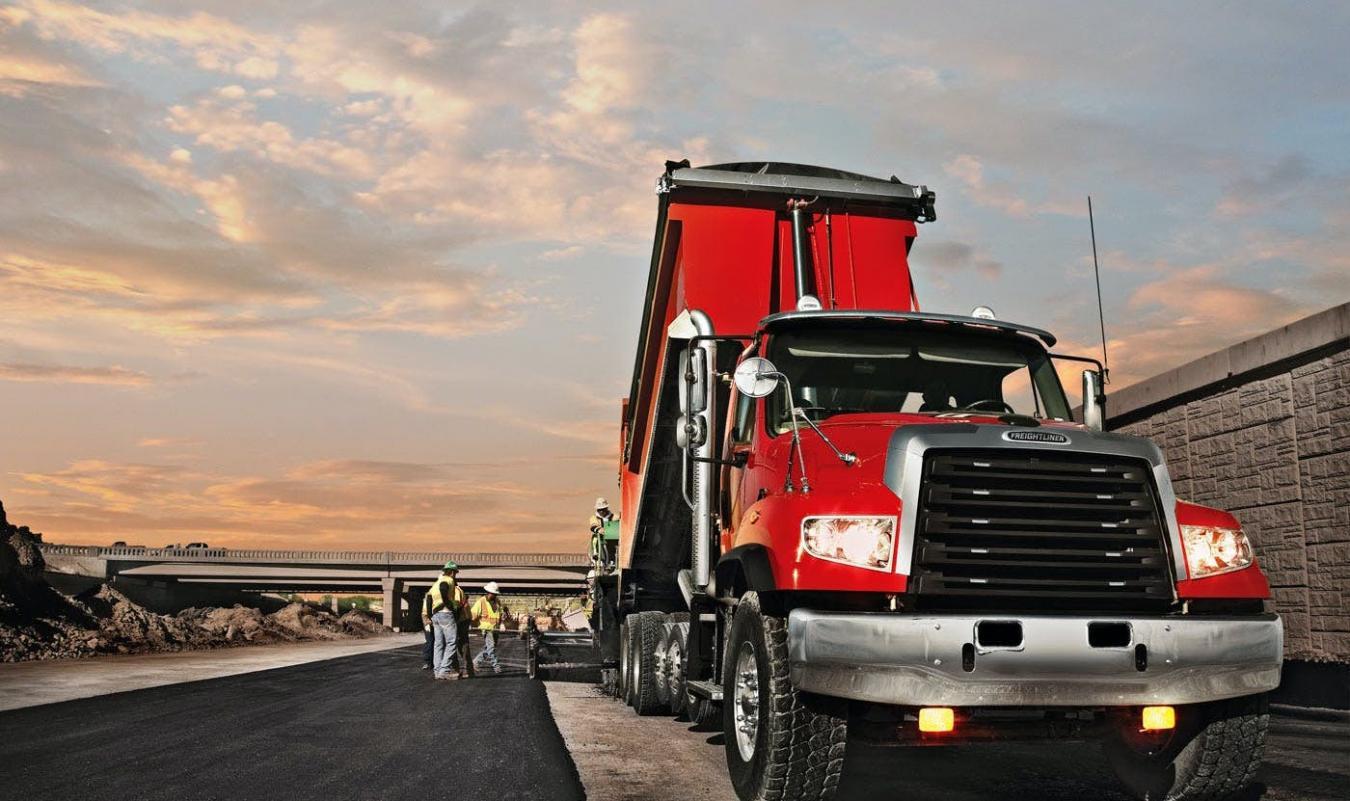 Red Freightliner dump truck on the side of the road with workers